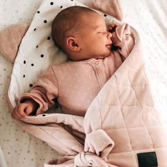 Sleeping newborn in a soft pink velvet swaddle blanket with bunny comforter in woven Moses basket
