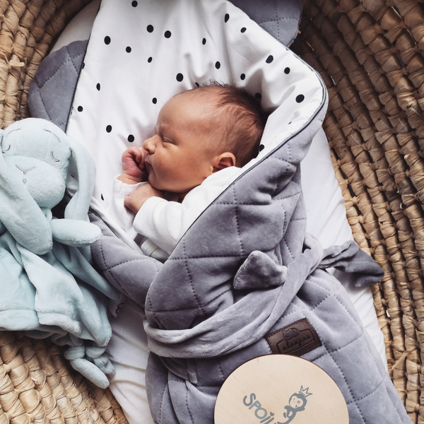 Newborn baby wrapped in Spoiltland bestselling grey velvet swaddle blanket in a Moses basket